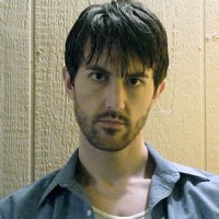 Kenny Ross Sullen man with dark hair and five o'clock shadow